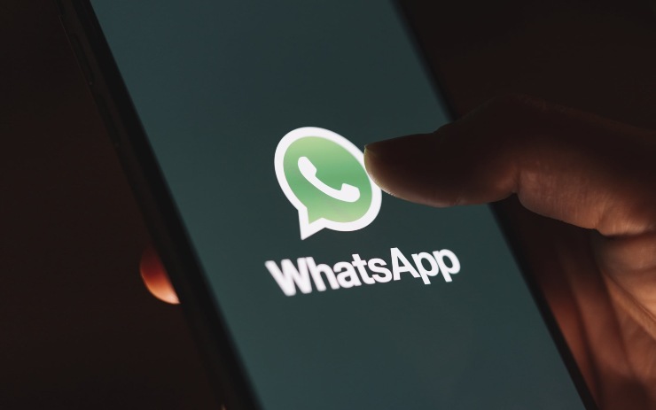 Smartphone in mano con logo WhatsApp e sfondo nero