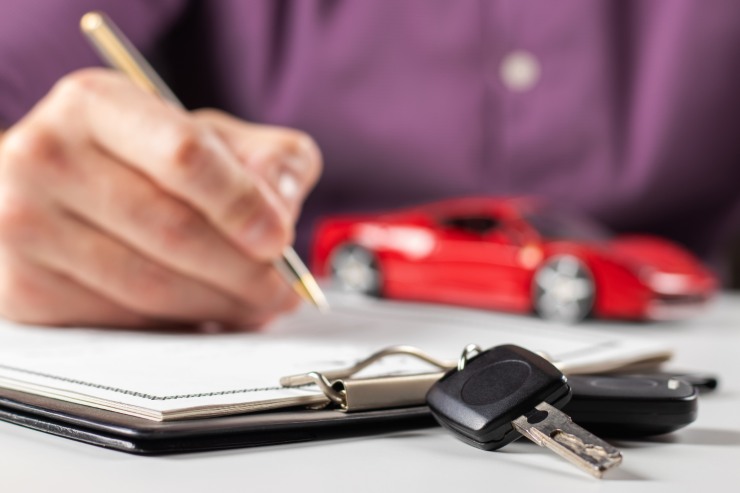 Uomo che compila documento per la vendita dell'auto. Piccola macchina e chiavi auto sul tavolo